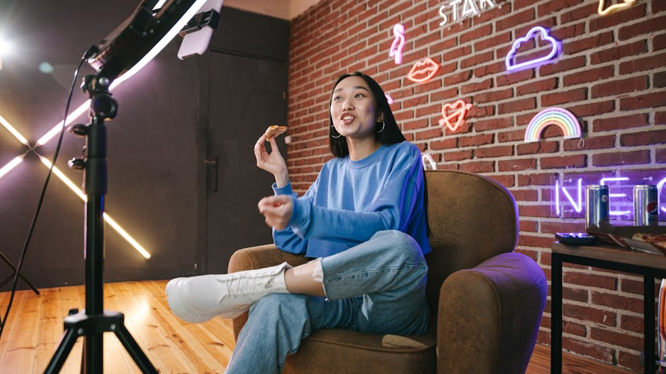 Young Asian woman streaming live indoors with neon lights, engaging audience through technology and creative content.